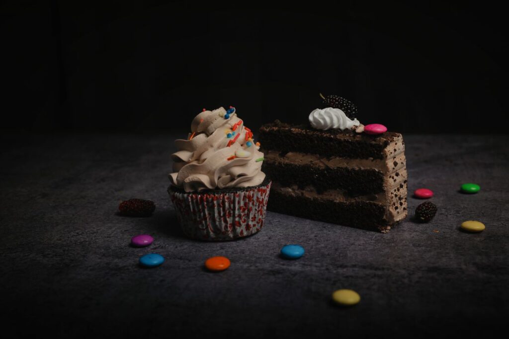Close-up of a chocolate cake slice and cupcake with sprinkles and candies, perfect for sweet cravings.